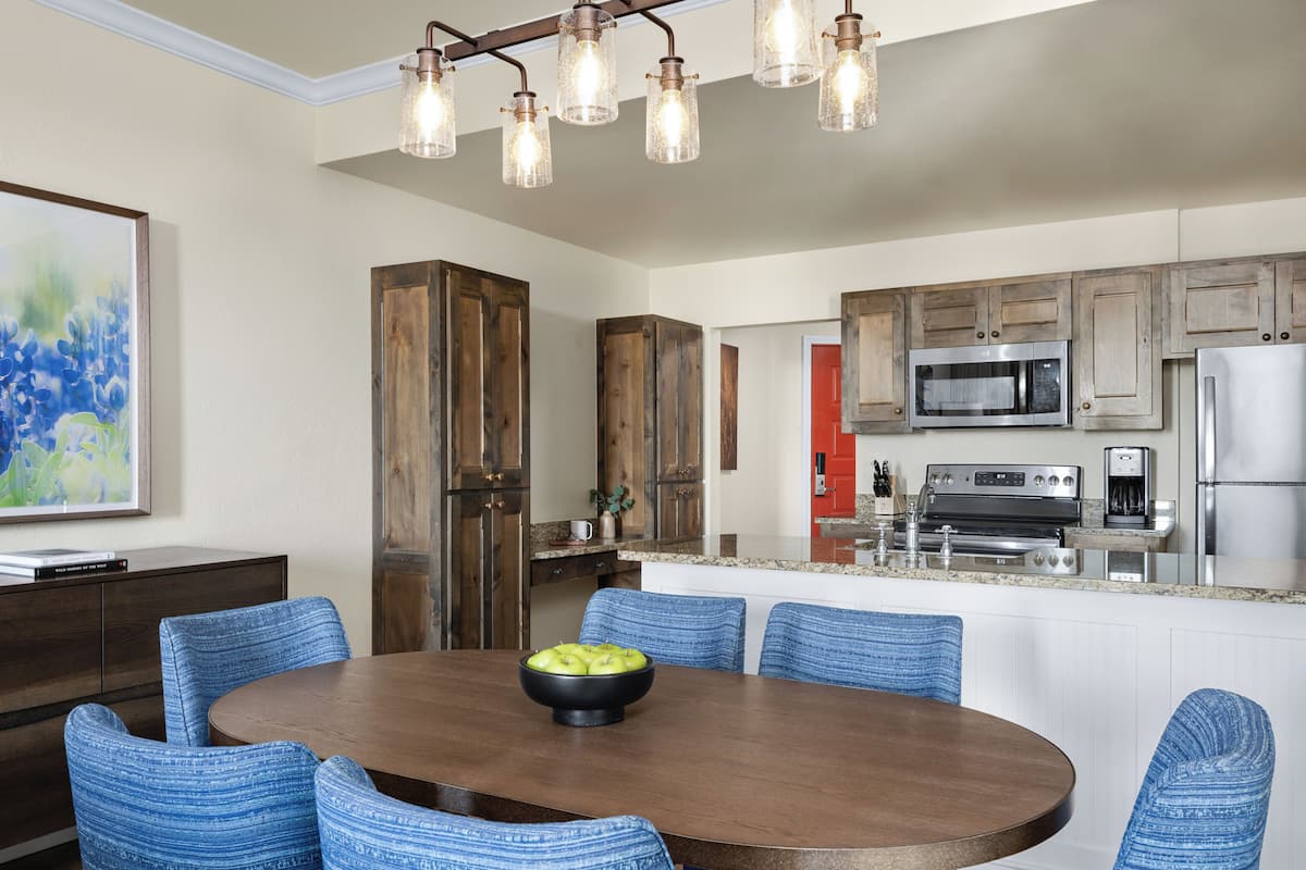 A modern kitchen with wooden cabinets, stainless steel appliances, and a dining area with blue upholstered chairs and a wooden table.