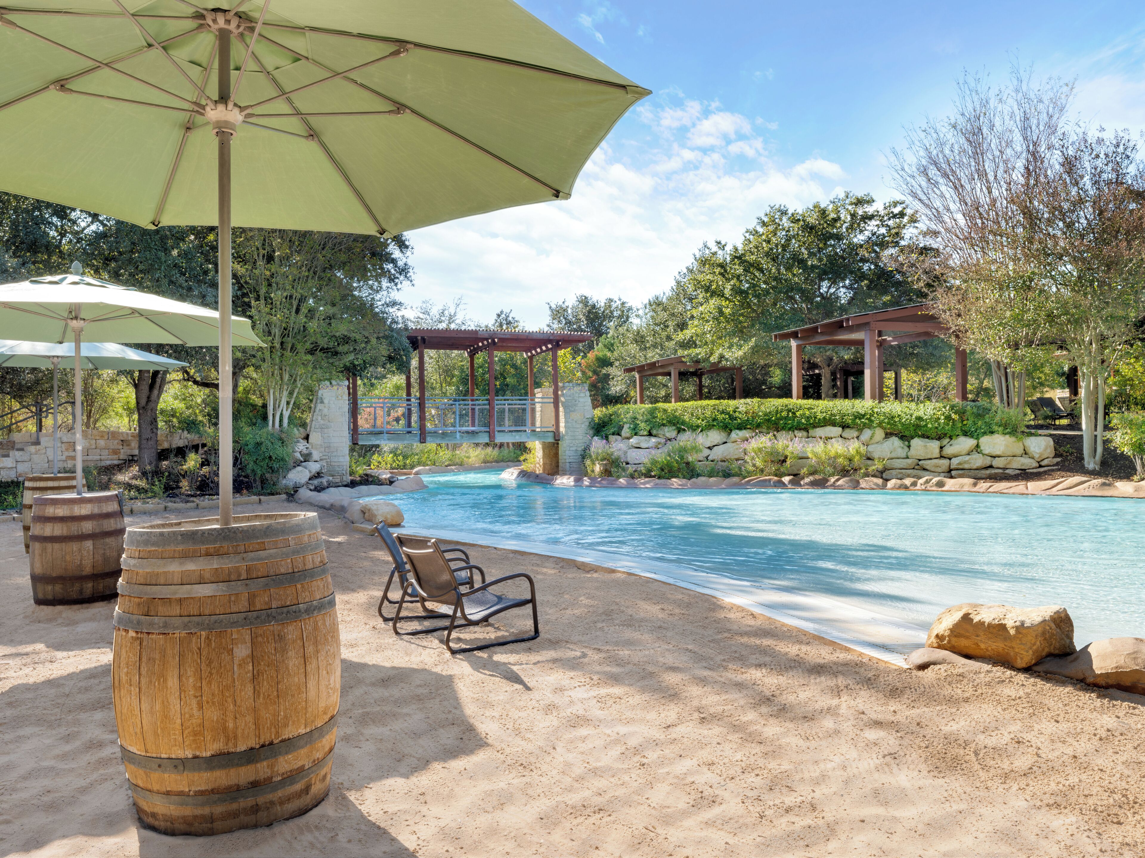 Un área de piscina con barriles de madera, sillas de descanso y una pérgola.