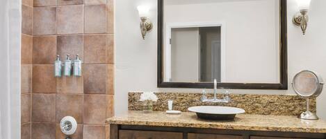 A bathroom with a shower, a sink, a mirror, and wooden cabinets.