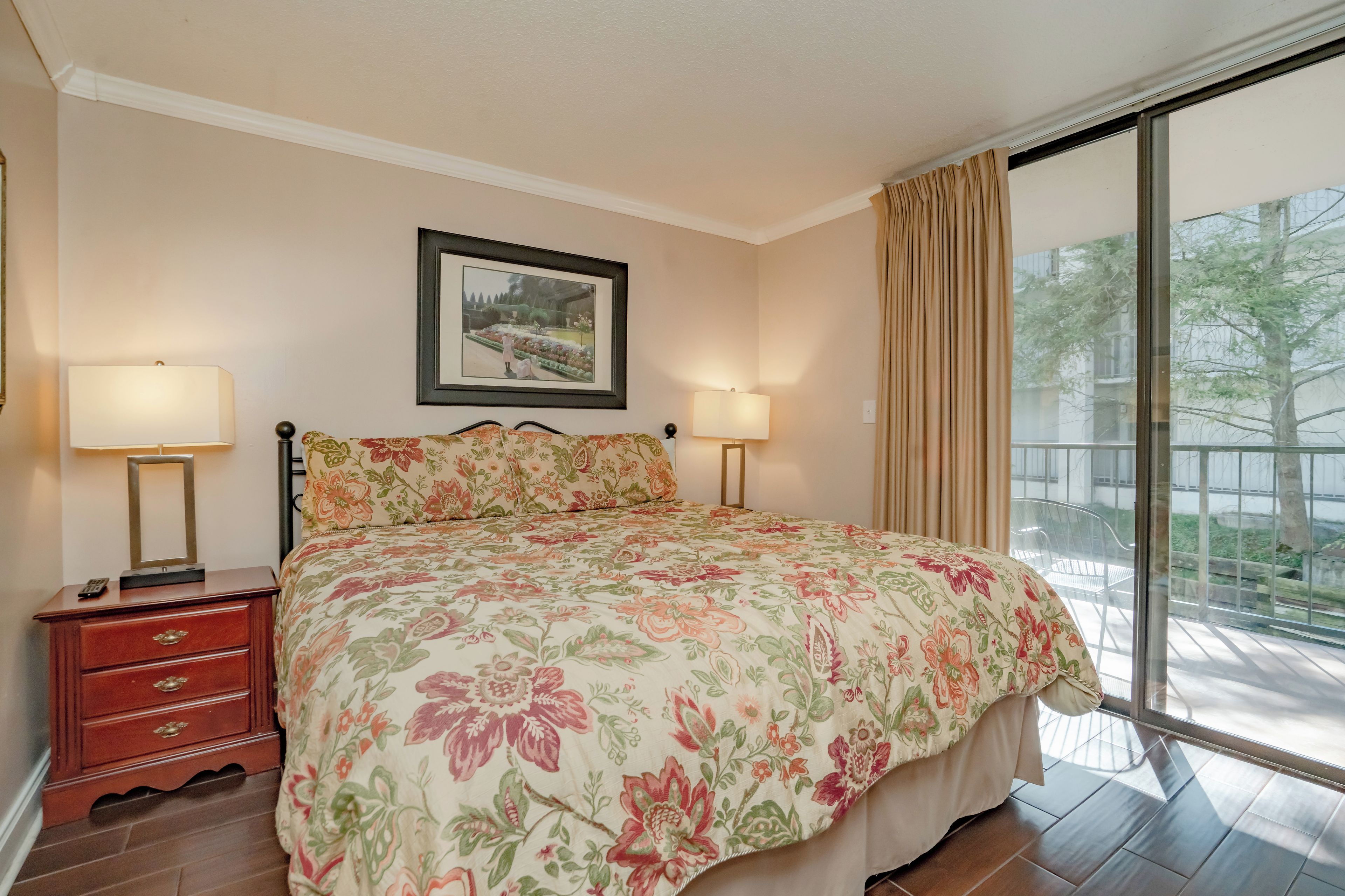A bedroom with a large bed, two bedside lamps, a nightstand, a dresser, and a framed picture on the wall.