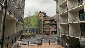 A multi-story building with balconies, a parking area, and a view of a mountain. - Oak Square Rentals (Gatlinburg)