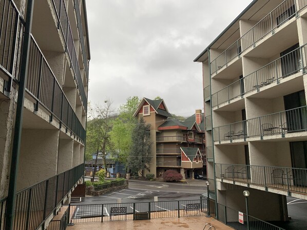 A multi-story building with balconies, a parking area, and a view of a mountain. - Oak Square Rentals (Gatlinburg)