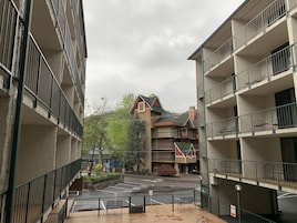 A multi-story building with balconies, a parking area, and a view of a mountain.