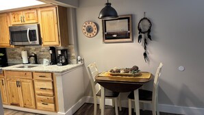 A kitchen with wooden cabinets, a microwave, a coffee maker, and a dining table with chairs. - Oak Square Rentals (Gatlinburg)
