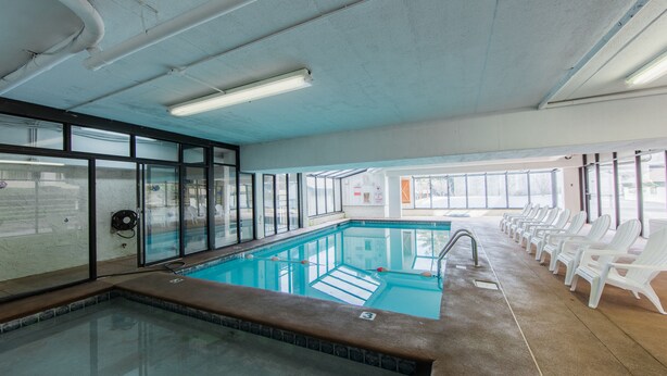 An indoor swimming pool with clear glass walls, a tiled floor, and white lounge chairs along the side. - Oak Square Rentals (Gatlinburg)