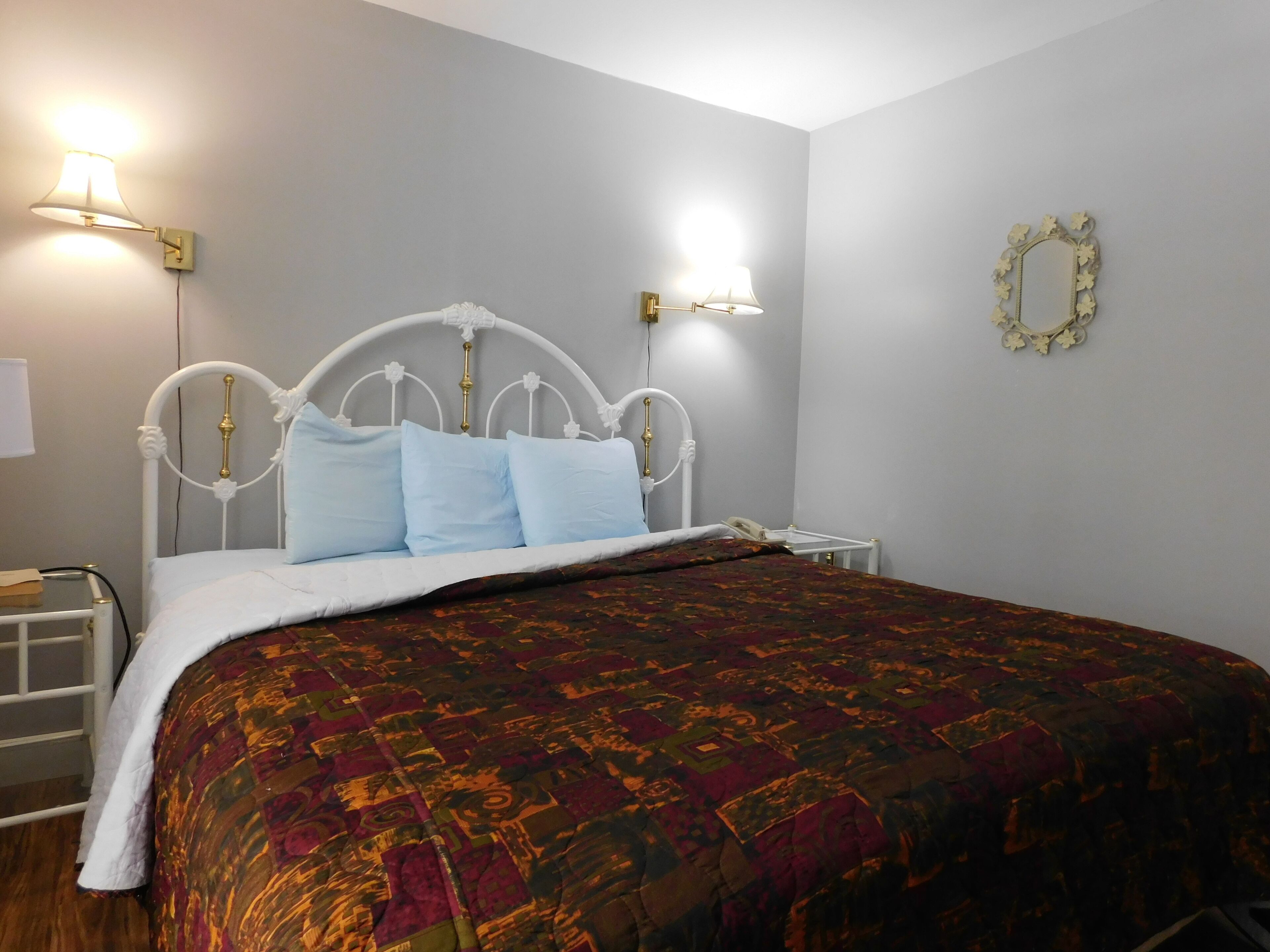 A neatly made bed with a patterned bedspread, a white metal headboard, and two bedside lamps.