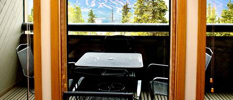 A balcony with a table and chairs, overlooking a mountainous landscape.