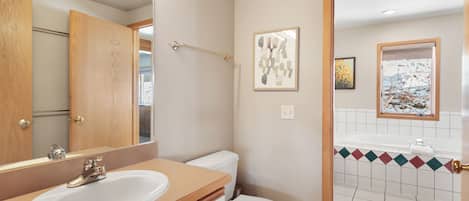 A bathroom with a wooden vanity, a white sink, a toilet, and a shower area.