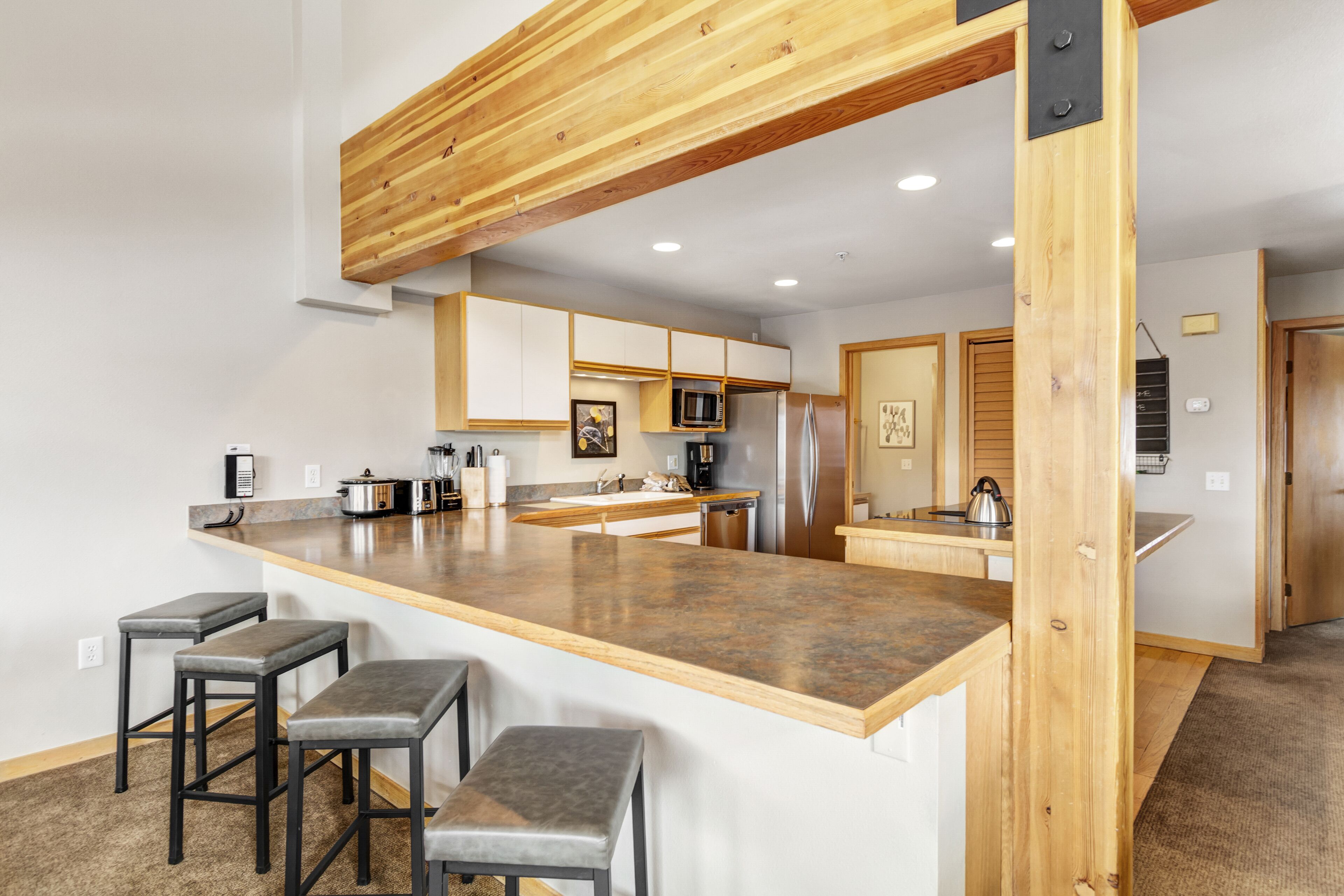 Une cuisine moderne dotée d’un îlot central, de tabourets de bar, de poutres en bois au plafond et de meubles de cuisine blancs.