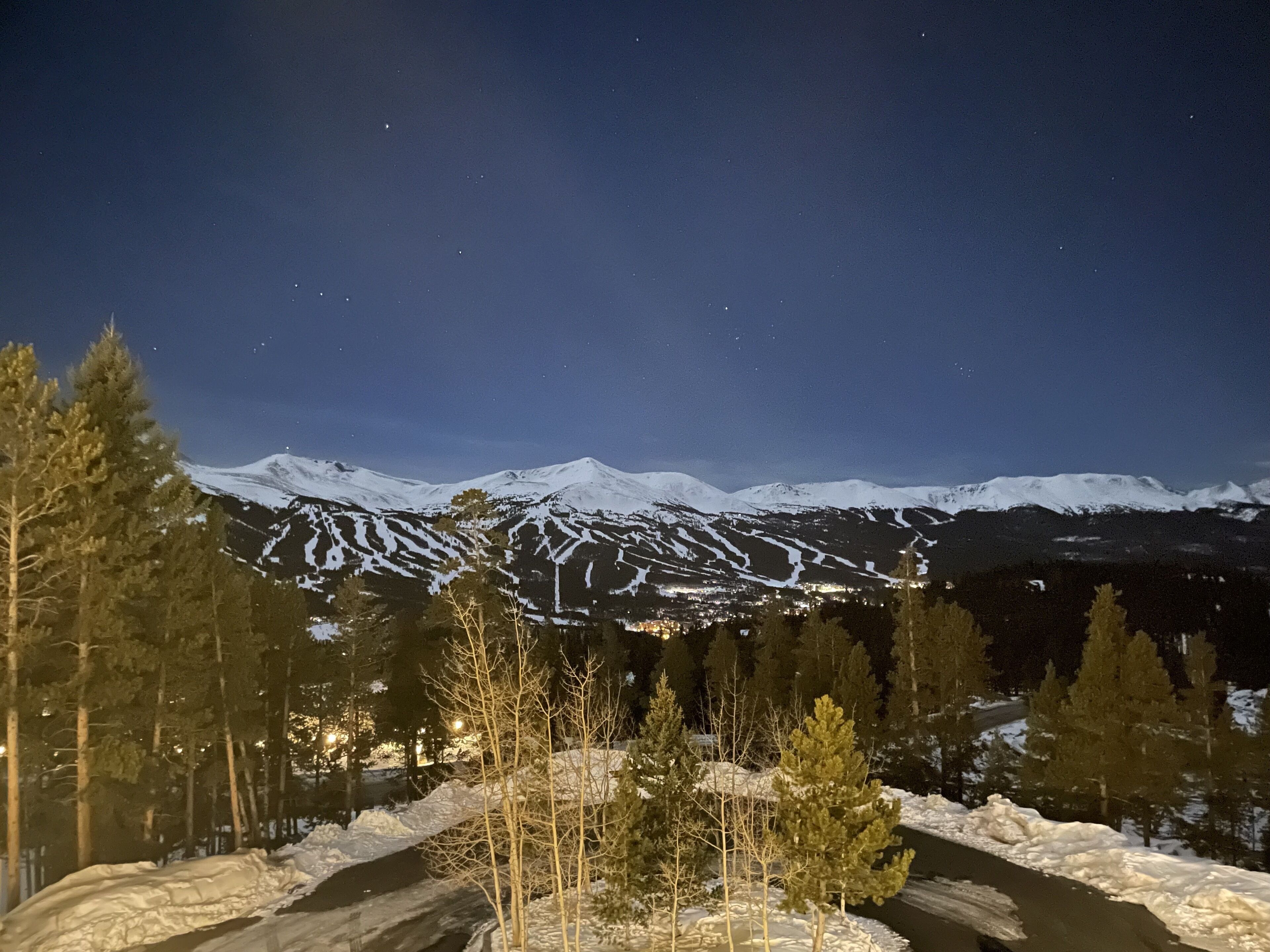 Un paysage montagneux enneigé de nuit, avec une vue dégagée sur les sommets et une route qui y mène.