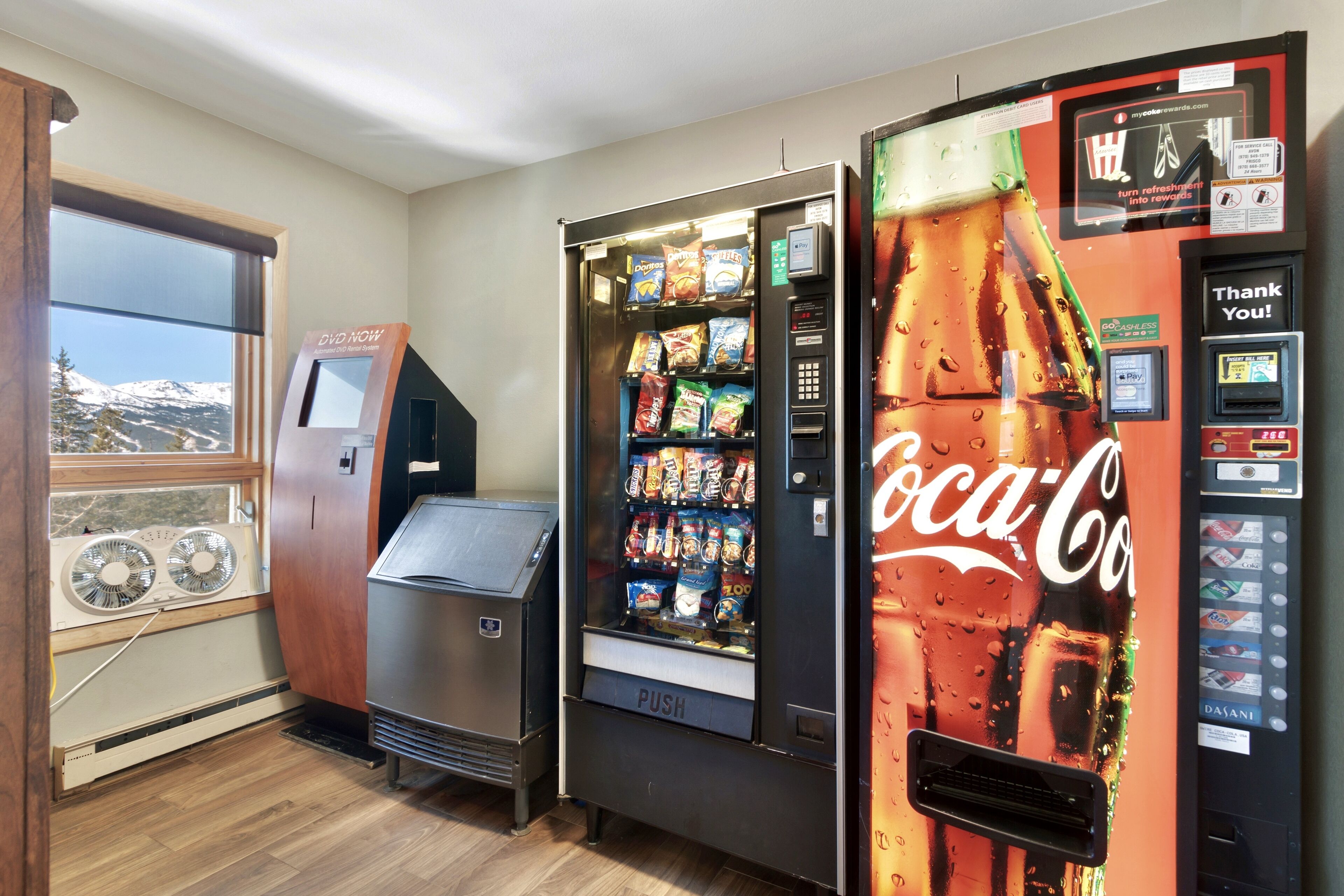 A room with a window, a DVD player, a vending machine, and a Coca-Cola refrigerator.