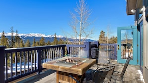 Une terrasse dotée d’un foyer extérieur, de chaises et offrant une vue sur des montagnes enneigées.