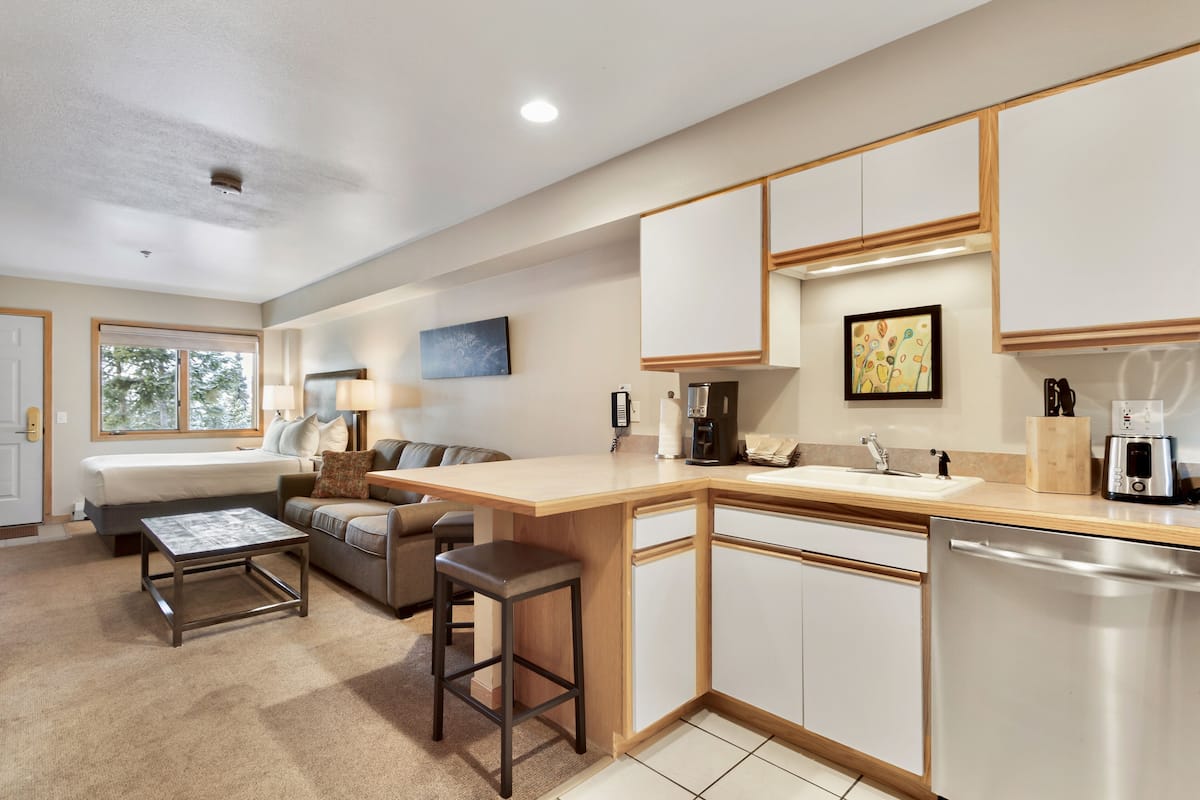A modern kitchen with a central island, built-in cabinets, and a dishwasher. There is a dining area with a table and chairs, and a living room with a sofa and a coffee table.