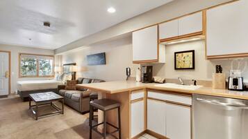 A modern kitchen with a central island, built-in cabinets, and a dishwasher. There is a dining area with a table and chairs, and a living room with a sofa and a coffee table.