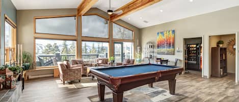 A spacious indoor area with a pool table, comfortable seating, large windows, and a view of the outdoors.