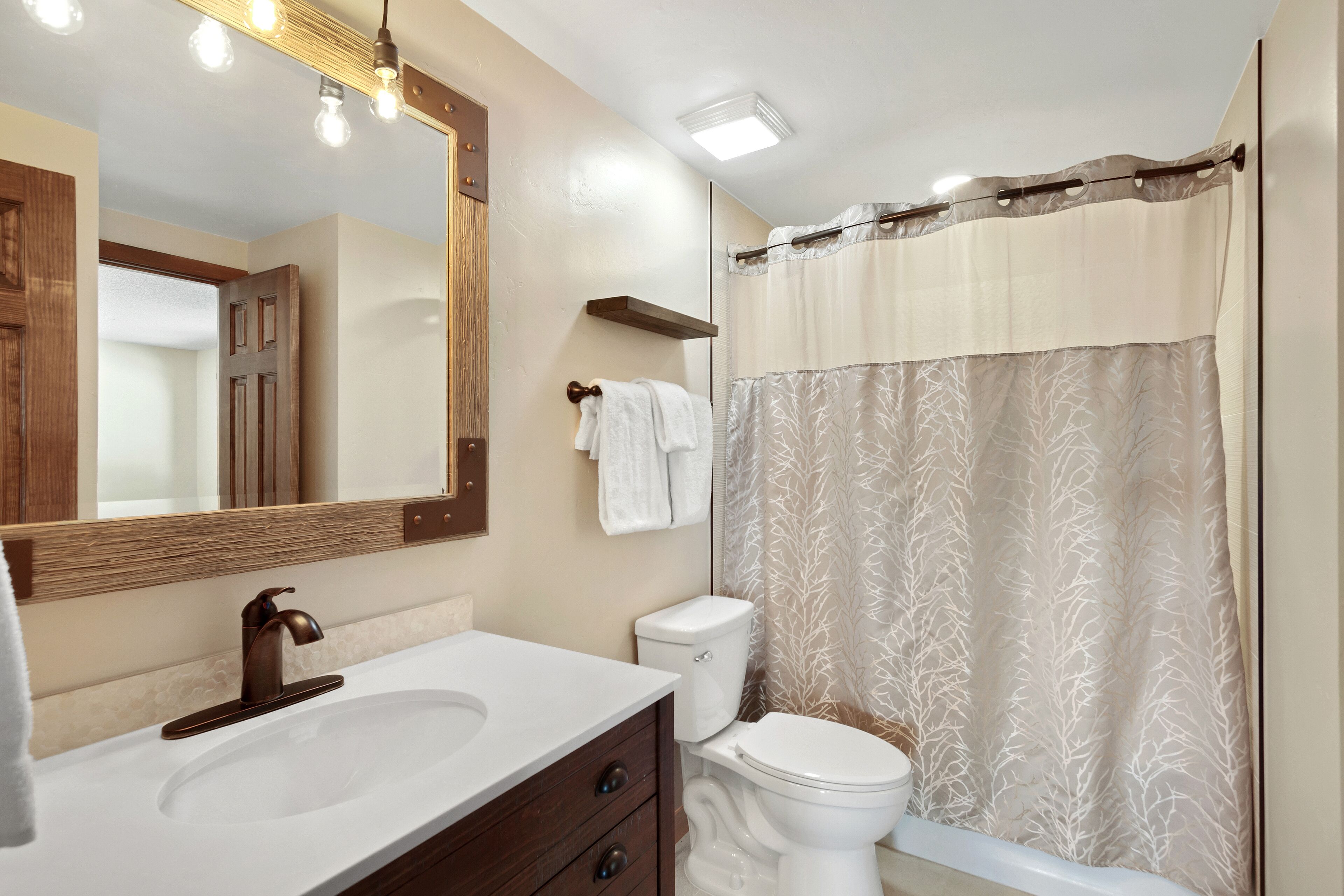 A bathroom with a sink, mirror, toilet, and shower curtain.