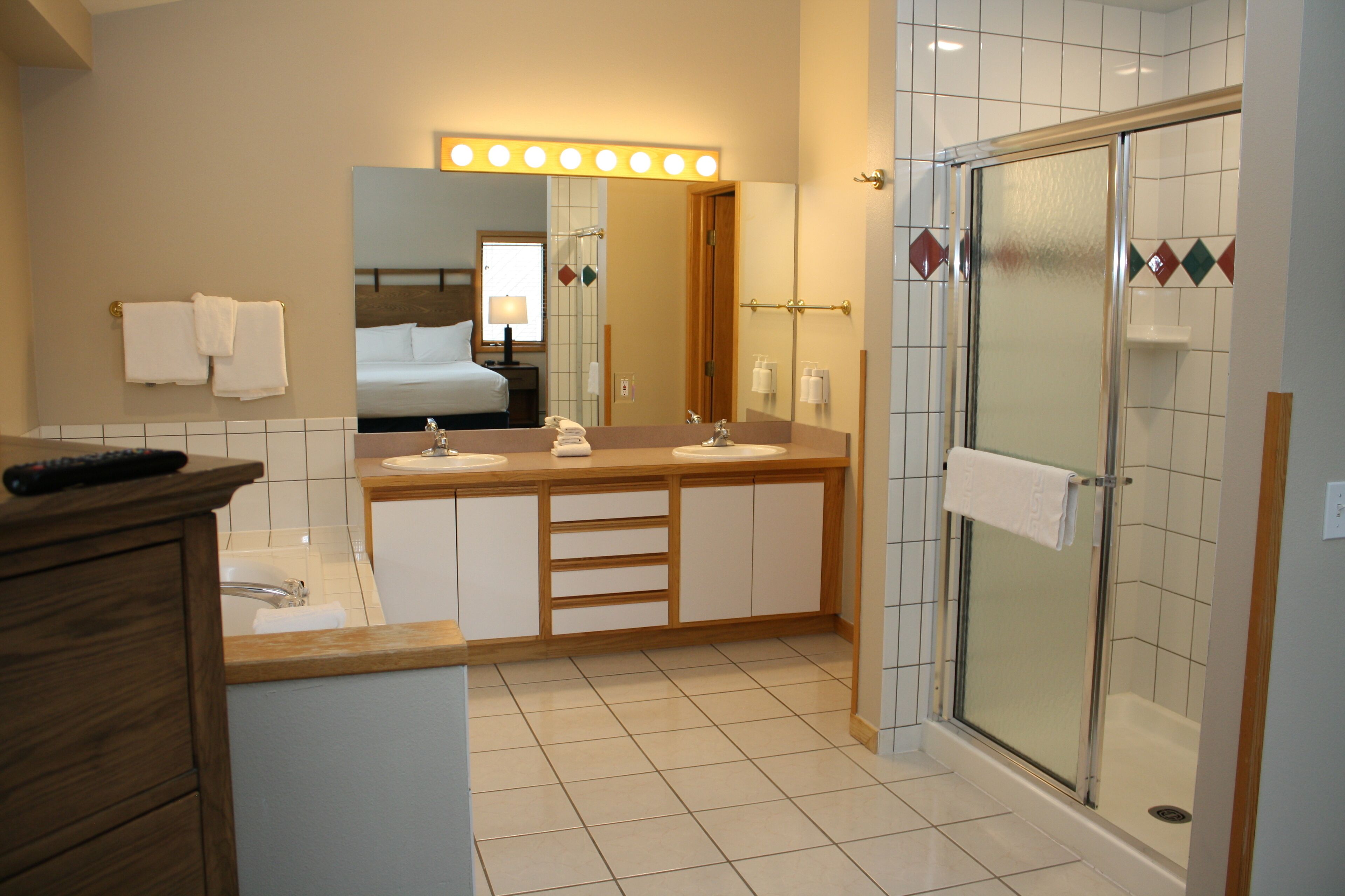 A modern bathroom with a vanity, a shower, and a large mirror with lights.