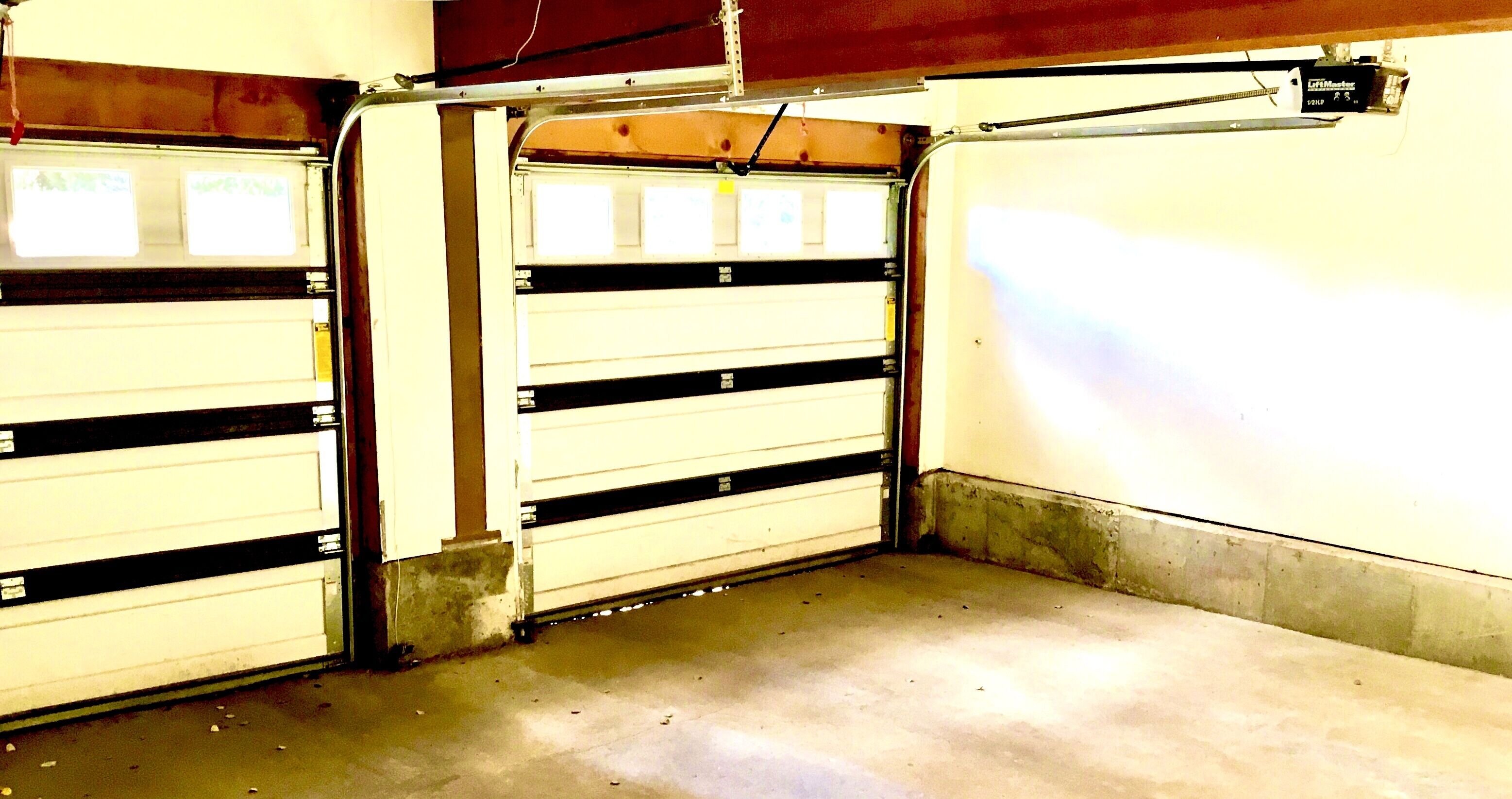 Un garaje con dos puertas cerradas, suelo de hormigón y una viga metálica sobre las puertas.