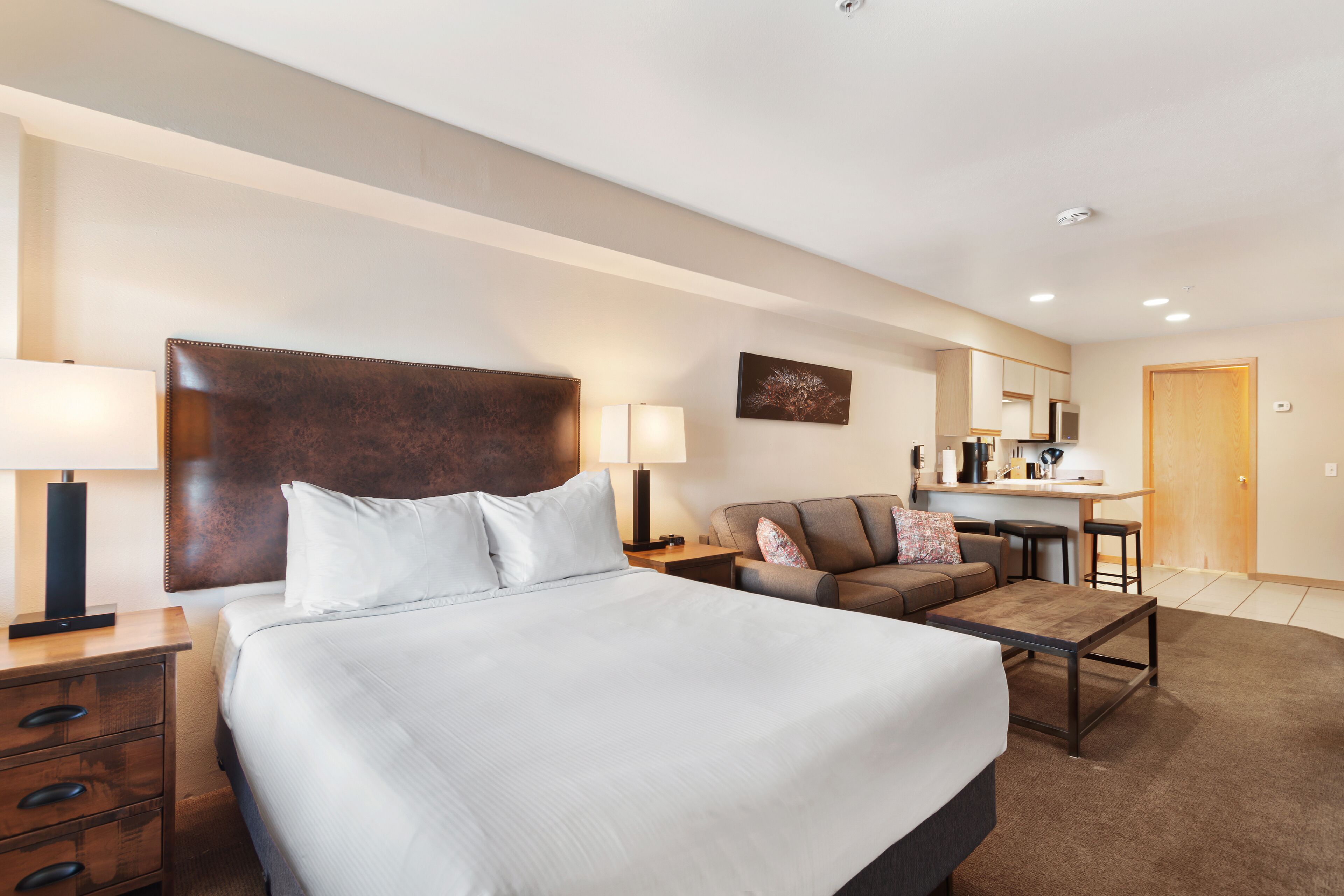 A hotel room with a large bed, a desk, a sofa, and a dining area.