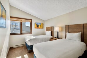 A hotel room with two beds, a window with a view, a painting, and a nightstand with a lamp.