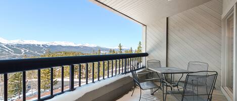 Un balcon avec vue sur des montagnes enneigées, une table avec des chaises et une rambarde.