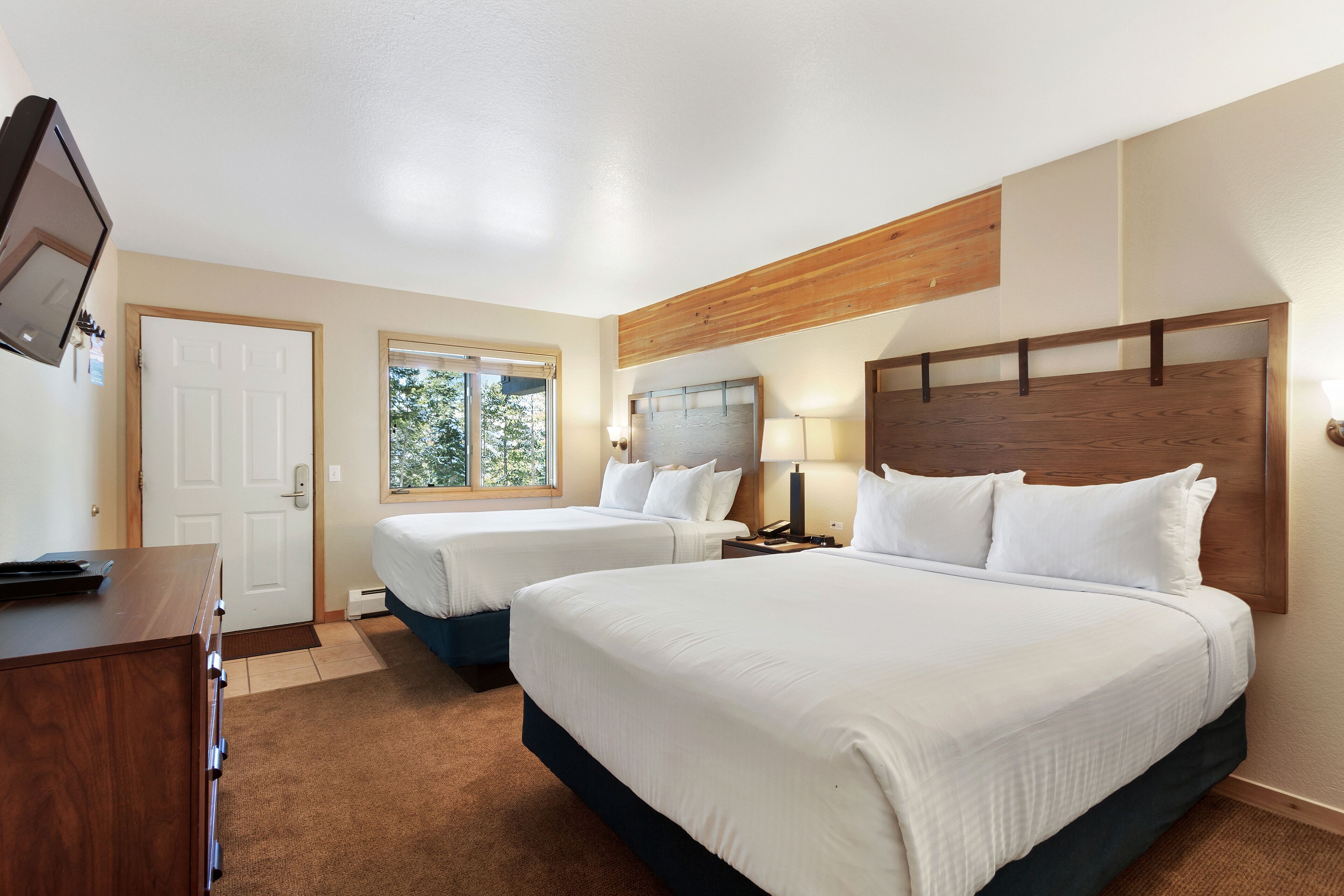 Quarto de hotel com duas camas, cabeceira de madeira, escrivaninha e televisão.