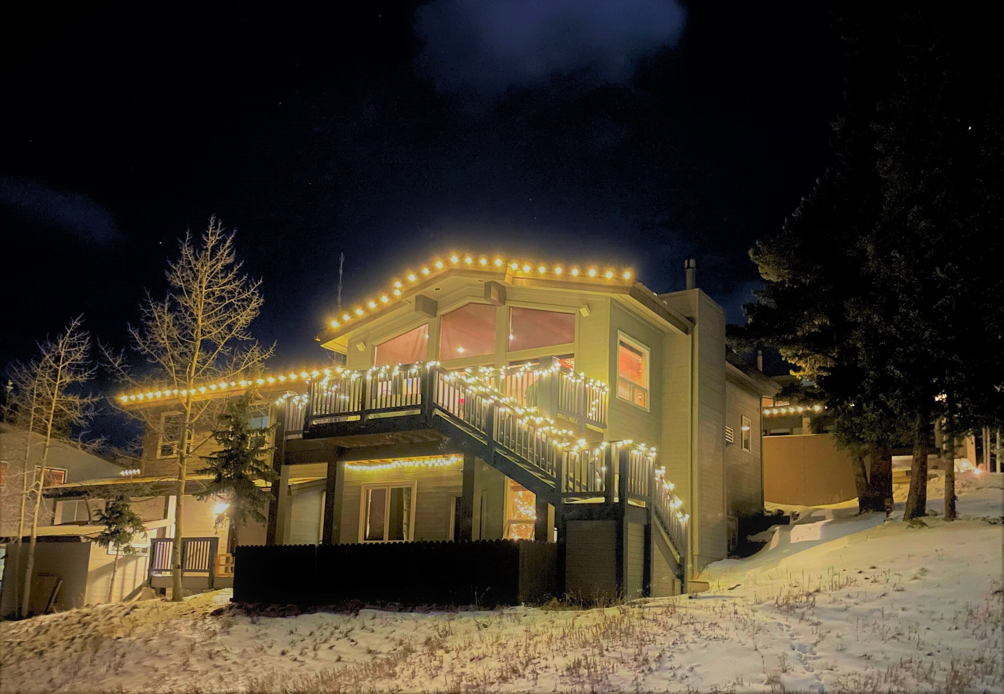 A two-story house with a balcony, snow on the ground, and string lights.