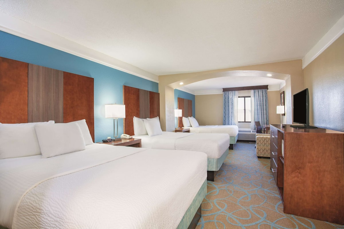 A hotel room with two beds, a TV, a desk, and a bathroom visible in the background.