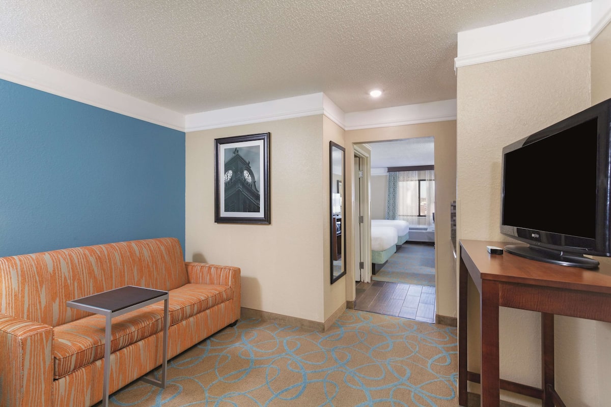 A hotel room with a sofa, a small table, a TV, and a bed in the background.