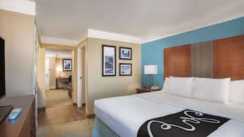 Habitación de hotel con cama, escritorio con lámpara, televisor y pasillo que conduce a un baño.