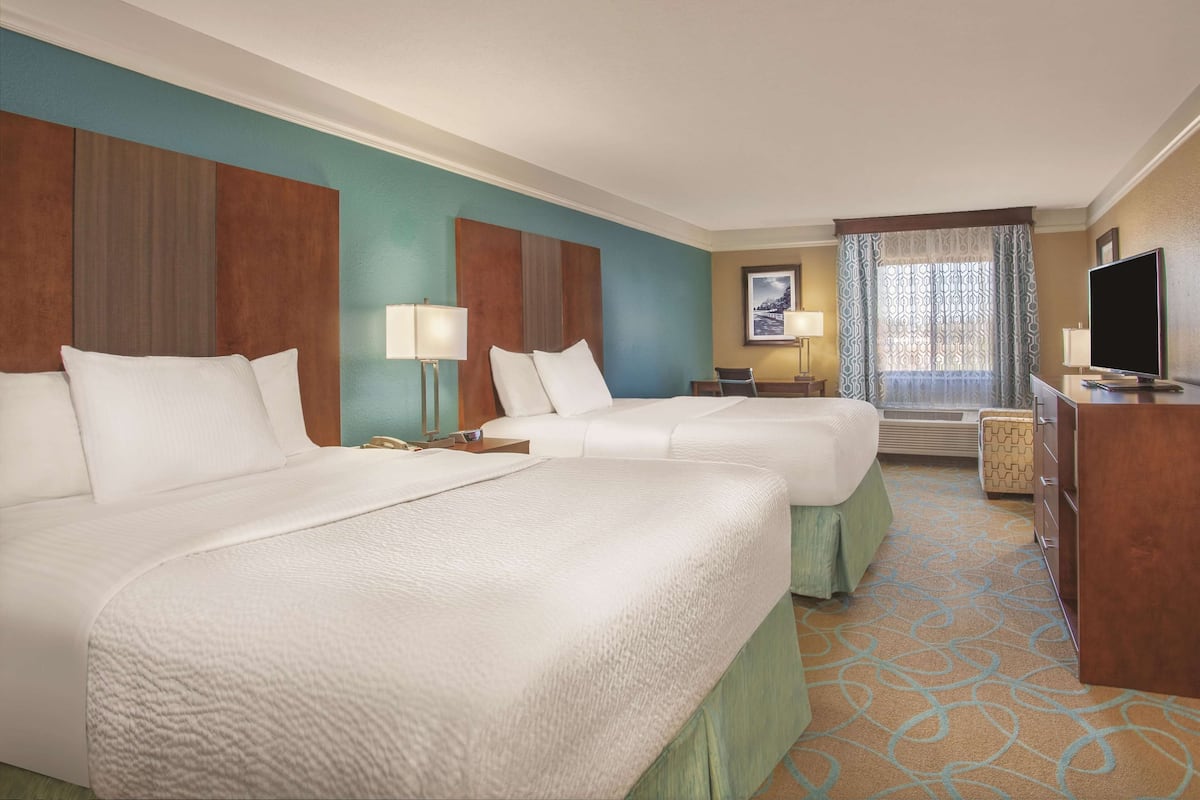 A hotel room with two beds, a desk, a television, and a window with curtains.