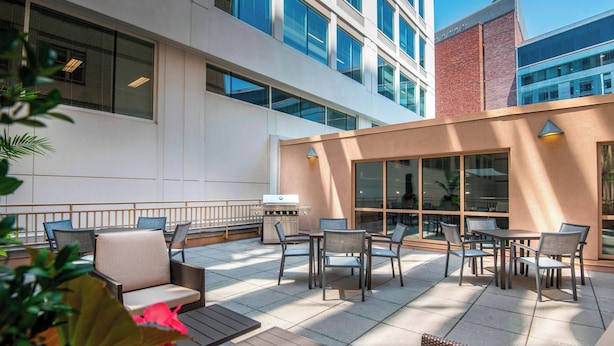An outdoor patio with seating and a grill area, surrounded by modern buildings.