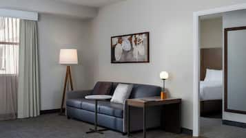 Habitación de hotel con sofá, una pequeña mesa redonda, lámpara, un cuadro en la pared y cama en una esquina.