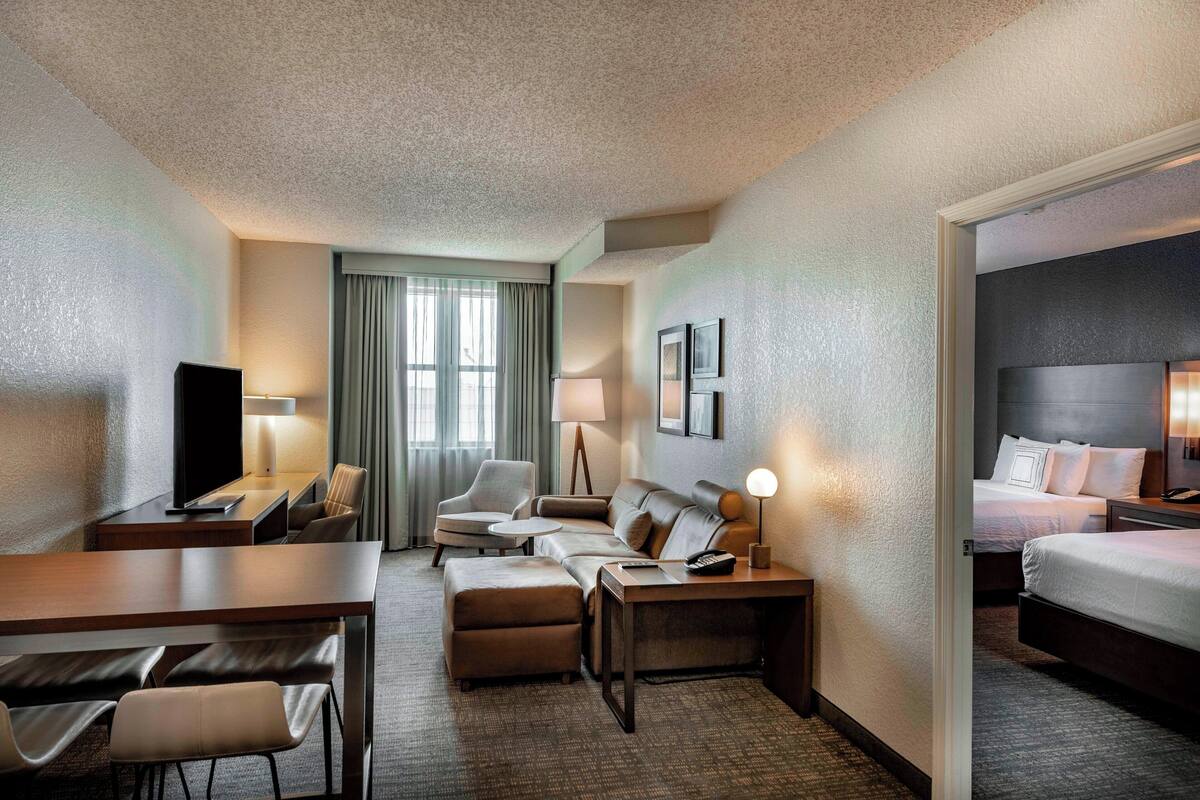 Habitación de hotel con sofá, escritorio, silla, cama y televisor.