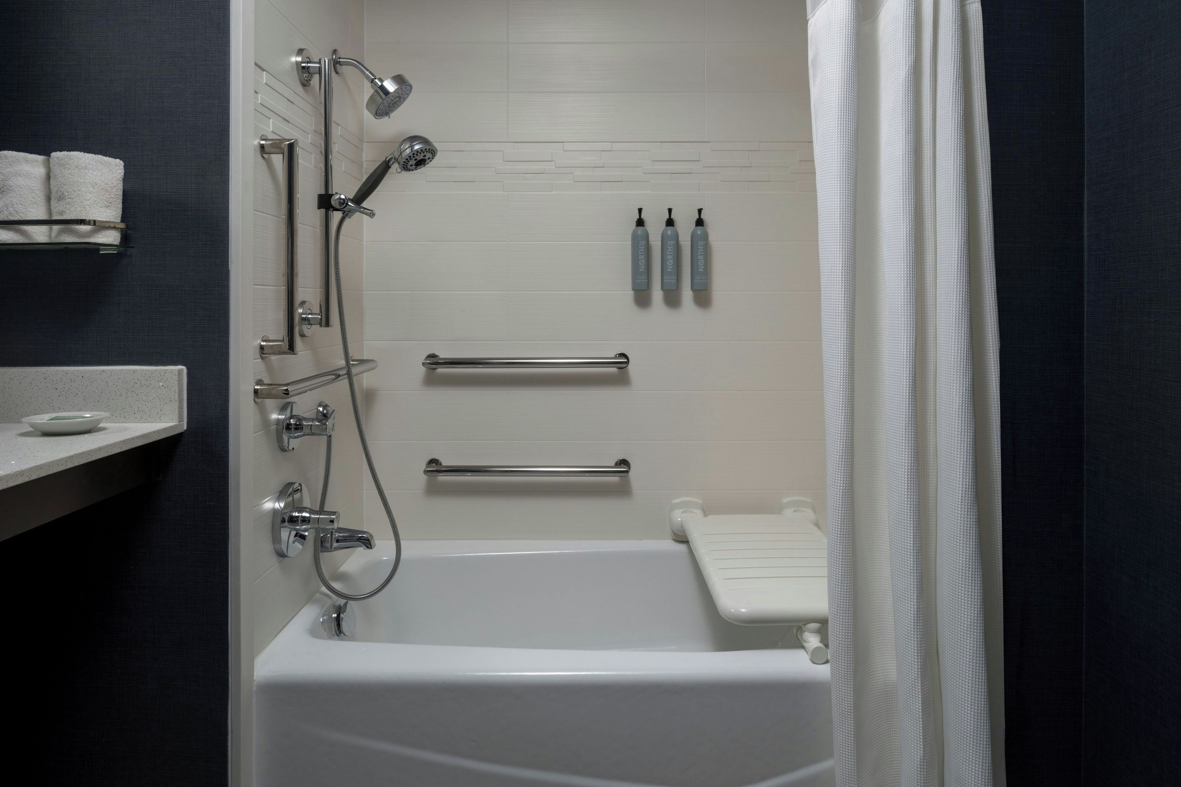 A modern bathroom with a bathtub, shower, and handrails.