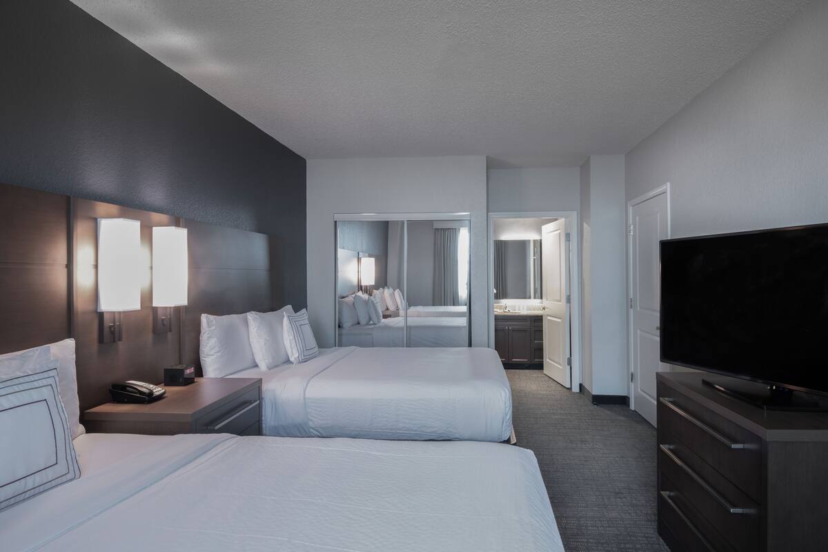 Habitación de hotel con dos camas, televisión, escritorio con lámpara y espejo.