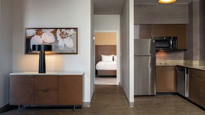 A modern hotel room with a kitchenette, a bed, and a hallway leading to another room.