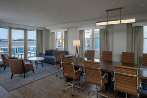 Ein Hotelzimmer mit großem Fenster, einer Sitzecke, einem Esstisch mit Stühlen und Blick auf die Stadt.