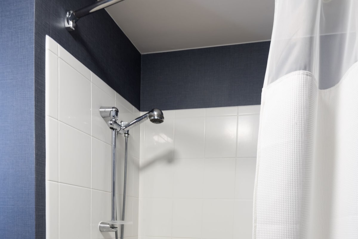 A modern bathroom with a bathtub, shower, and handrails.