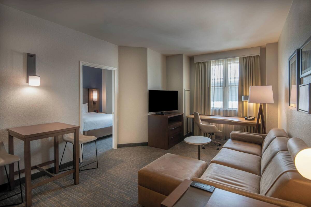 Habitación de hotel con cama, escritorio con computadora, televisión, sofá y una mesita.
