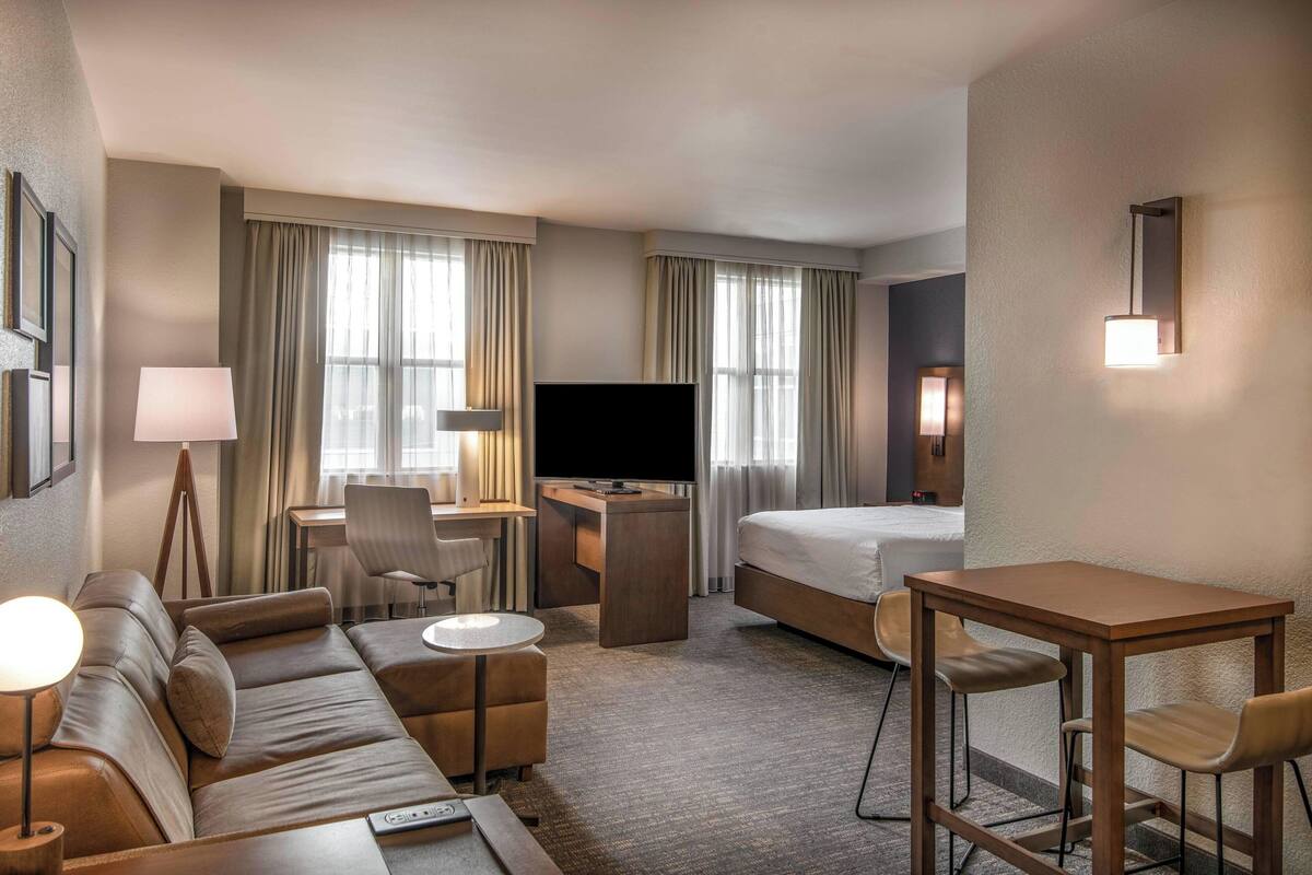 Una habitación de hotel con sofá, escritorio con televisor, cama y una pequeña mesa con sillas.