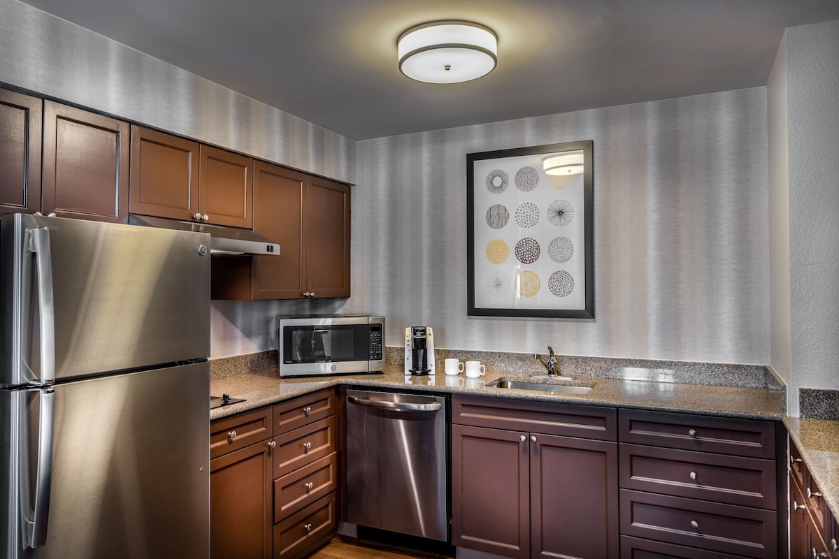 A modern kitchen with stainless steel appliances, wooden cabinets, and a granite countertop.