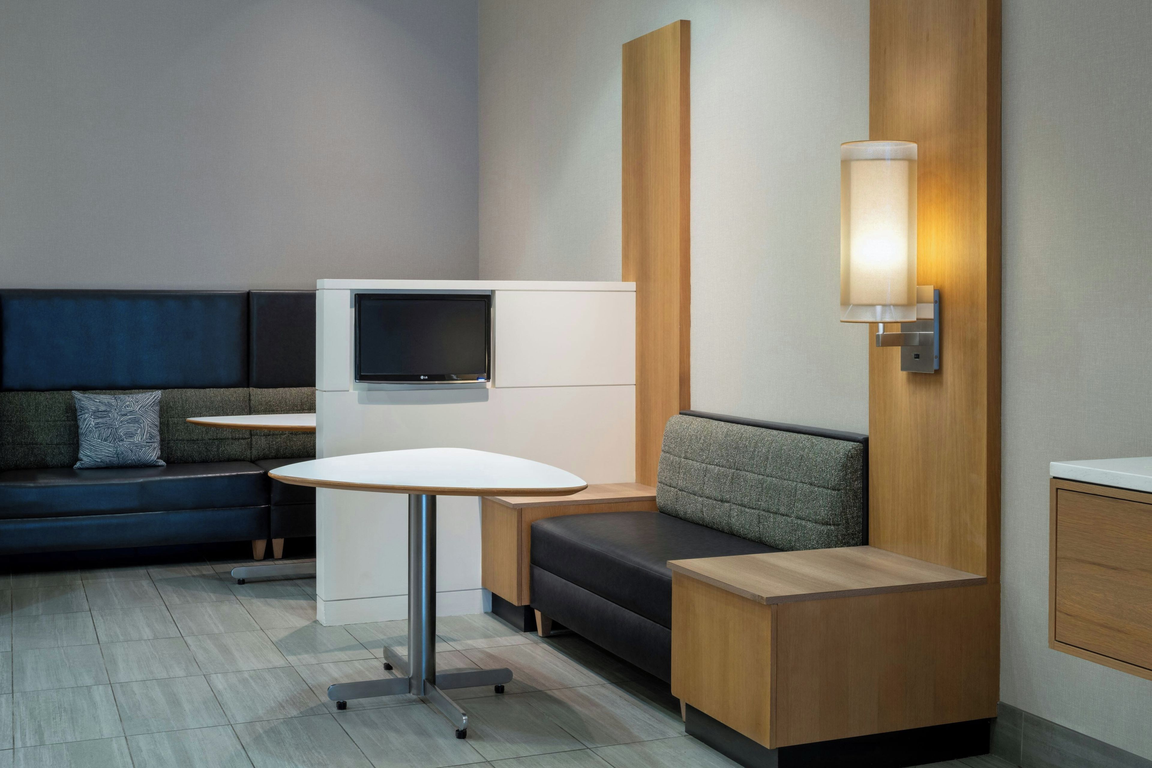 A modern hotel room with a sofa, a small table, a TV, and a wall-mounted light.