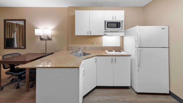 Cocina compacta con armarios blancos, microondas, refrigerador, pileta y comedor con mesa y sillas.