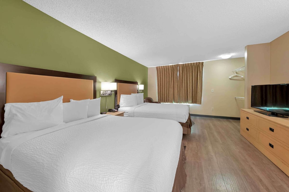 A hotel room with two beds, a TV, a dresser, and a window with curtains.