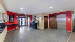 Vestíbulo de hotel con mostrador de recepción, estación de café y dos ascensores.