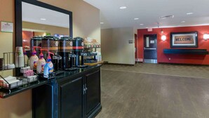 Zona de recepción con estación de café, un cartel de bienvenida y una señal de salida.