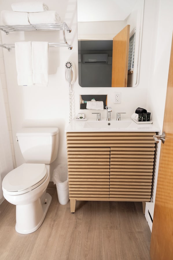 Un baño moderno con inodoro blanco, tocador de madera y espejo sobre el lavabo.