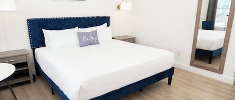 Un llit ben fet amb capçalera blava, una taula de nit, una làmpada i un quadre a la paret.