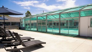 A covered outdoor pool area with lounge chairs and a glass-enclosed structure. - Endless Dunes, A Modern Motel (Eastham)